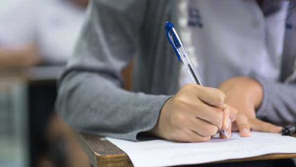 Estudante, sentado em carteira, redigindo a redação do Enem.
